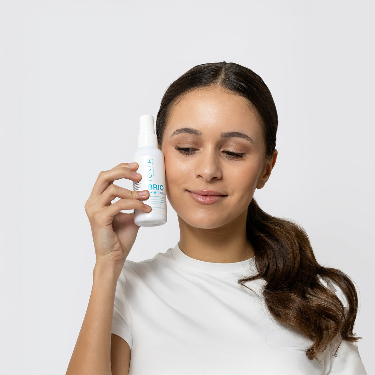 Young woman holding a bottle of Skin Renew Toner next to her cheek. Her expression is calm as Skin Renew Toner soothes skin while reducing redness and impurities.